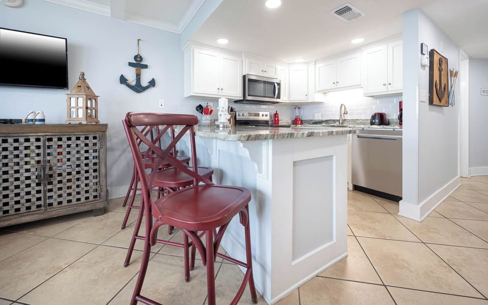 The kitchen features stylish red stools, modern appliances, and a charming coastal decor for a delightful cooking experience