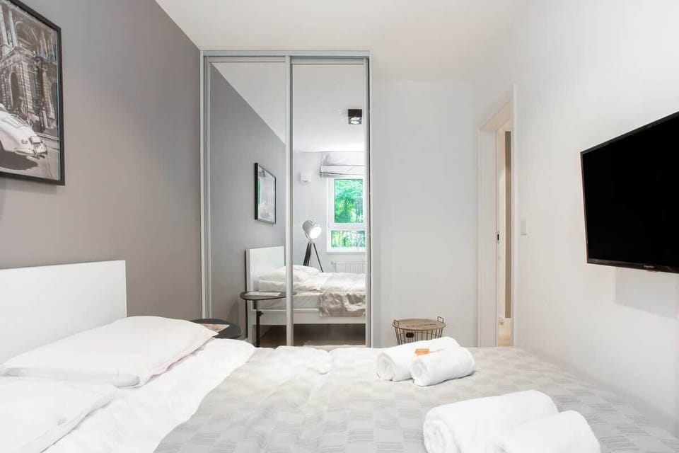 A cozy bedroom with a minimalist design, featuring a neatly made bed, a TV on the wall, and a small side table, providing a peaceful space for relaxation.