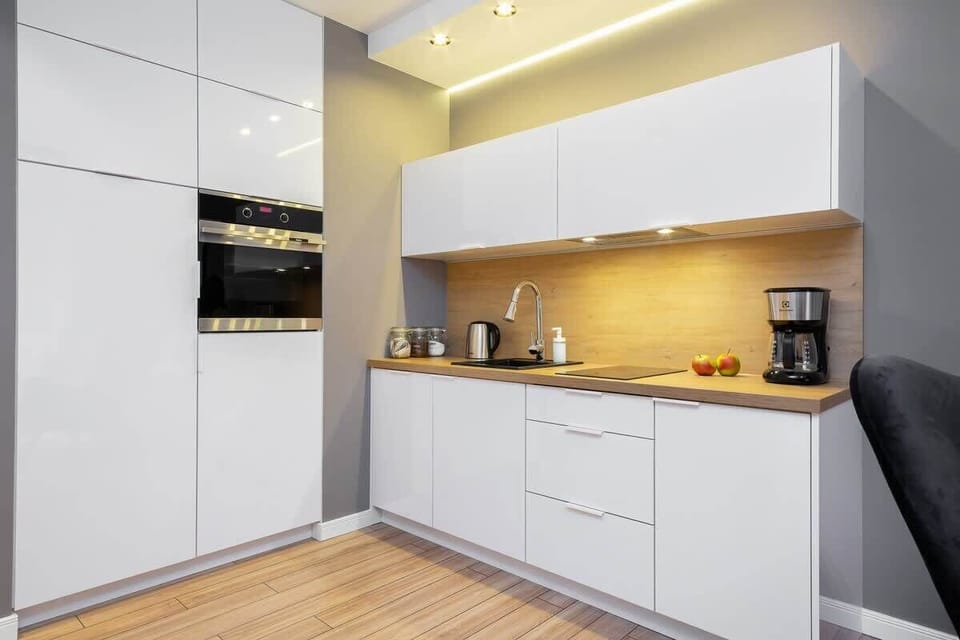 A modern, white kitchen with glossy cabinets, wooden accents, and under-cabinet lighting, creating a functional and stylish cooking area.