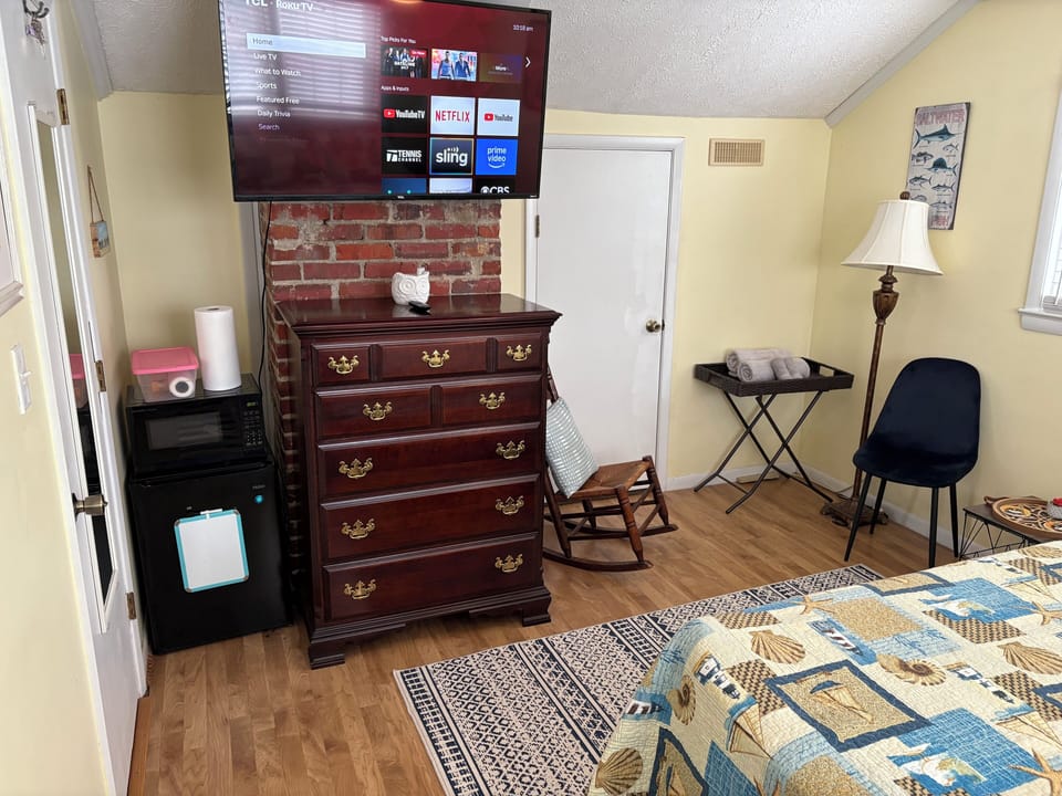 Wall mounted tv, microwave, refrigerator, and seating in queen room.