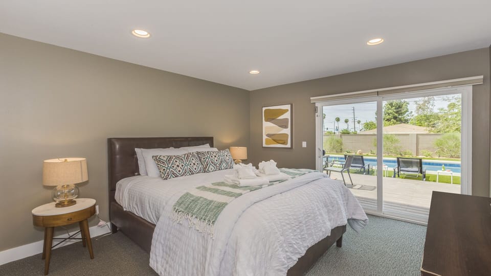 - King bedroom with plush bedding and direct pool view   - Sliding glass doors open to relaxing outdoor area   - Warm lighting creates restful evenings and mornings