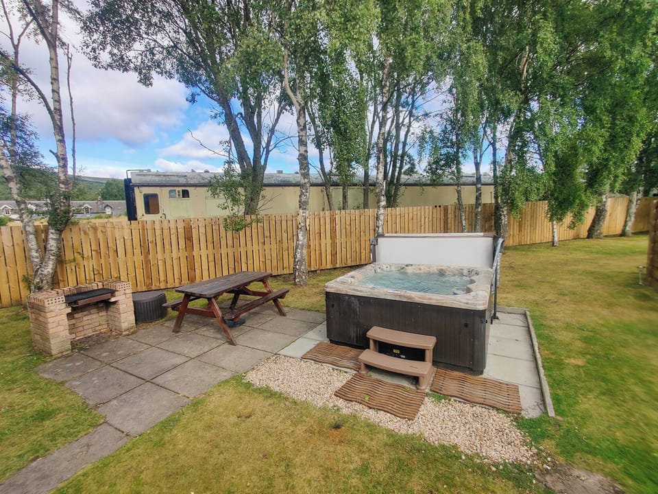 Garden area with hot tub and some vintage Strathspey Steam Railway stock in the background | Holly Lodge, Aviemore