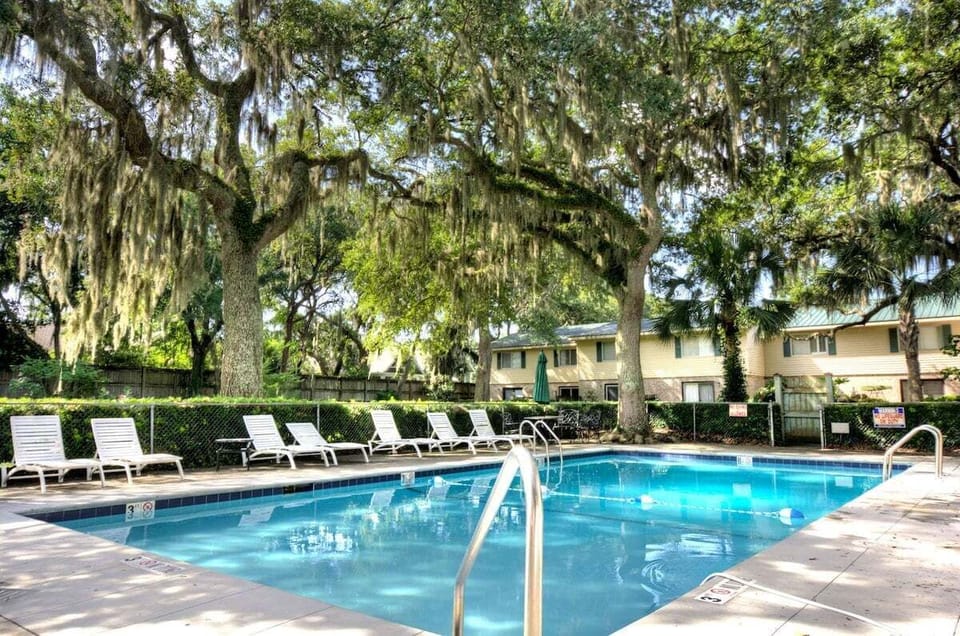 Community pool with lounge chairs and moss-draped oaks