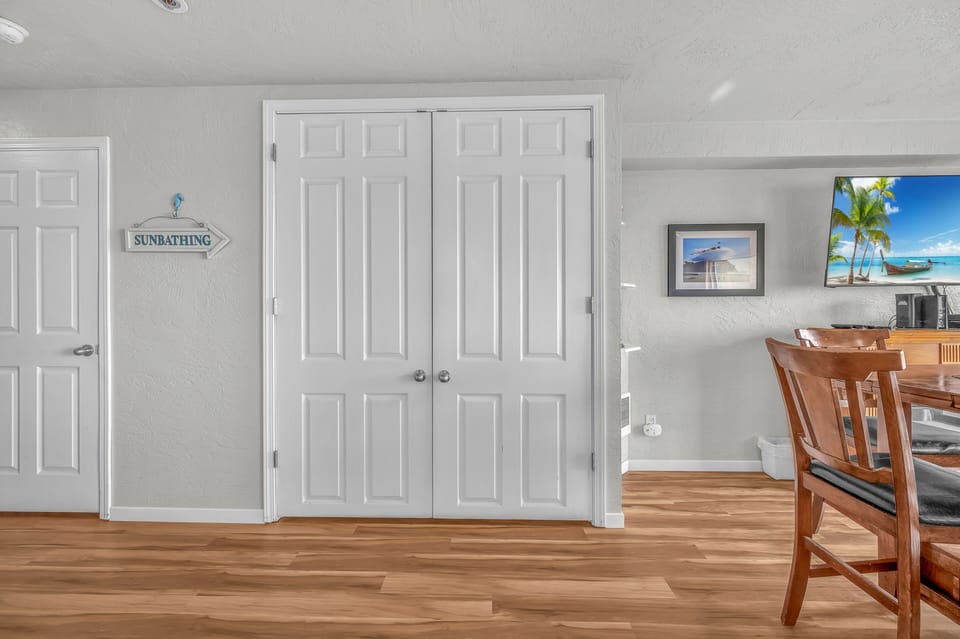 Your bright dining space features warm wood floors, tropical artwork, and a charming 'sunbathing' sign pointing to your beach adventures.