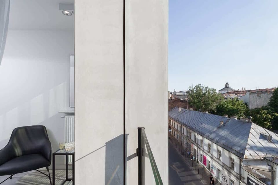 A cozy balcony with a glass railing, offering a view of the city. It has space for a small table and chairs, perfect for enjoying fresh air.