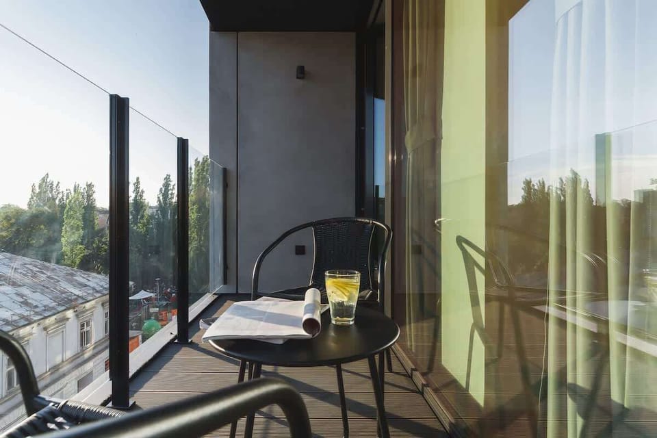  A small balcony area set up with a round table and two chairs, perfect for enjoying outdoor dining or coffee. The view shows neighboring buildings.