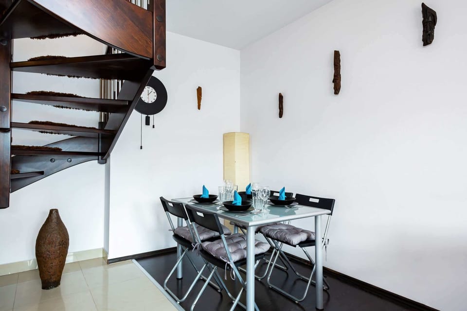 A dining area in the living room, featuring a stylish glass table with modern chairs, a vase of fresh flowers, and minimalist wall decor for a touch of elegance.