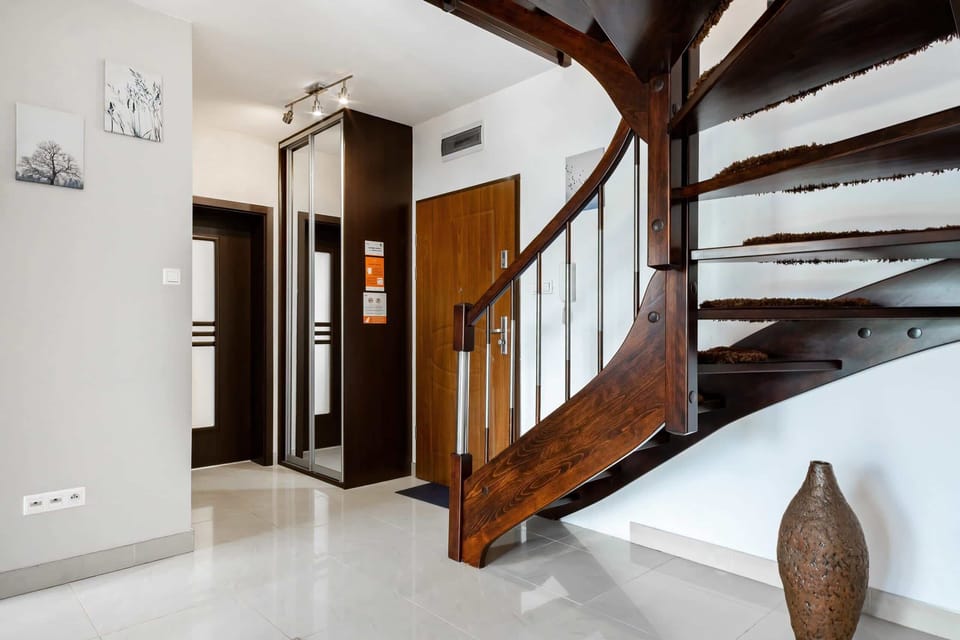 A modern hallway with light gray floors, sleek finishes, and a wooden staircase leading to the upper level, giving a clean and sophisticated appearance.