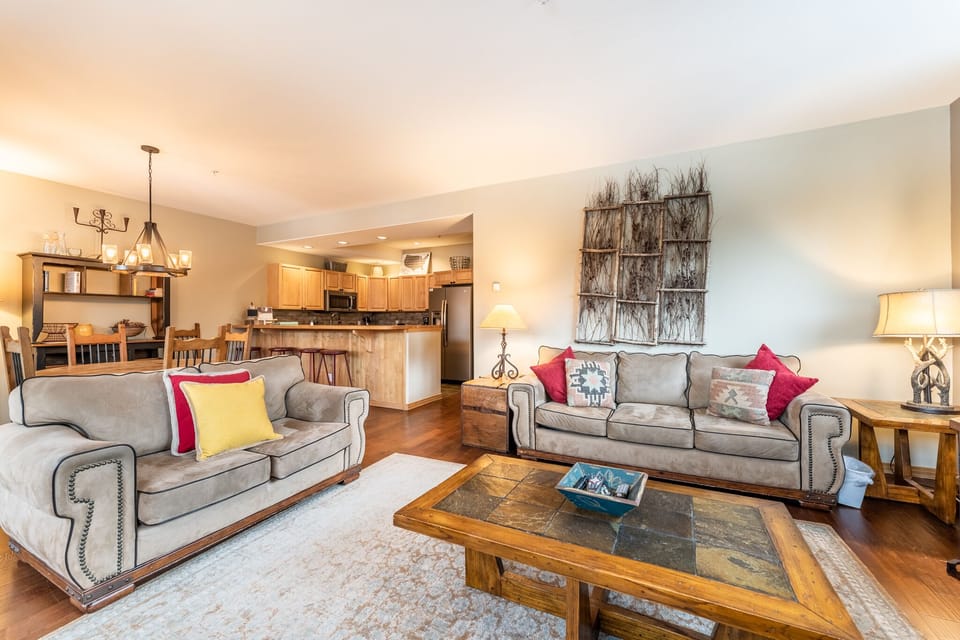 Relax in your spacious open-concept living area with plush gray sofas, rustic touches, and a fully equipped kitchen perfect for home-cooked meals.