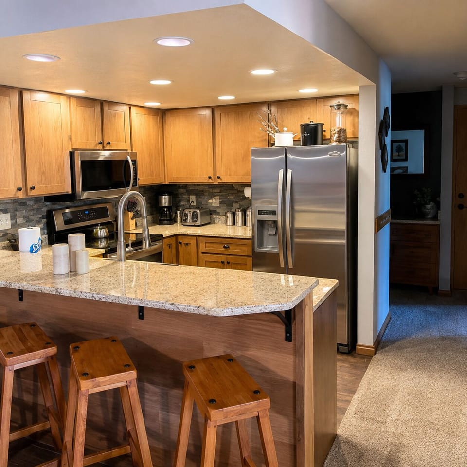 Your fully equipped kitchen invites you to cook and gather around the granite breakfast bar, with modern stainless appliances and warm wood cabinetry creating a welcoming space for meals together.