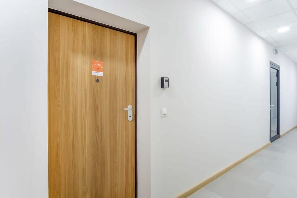  The main entry door to the apartment, located in a bright hallway with clean white walls and light wood flooring.