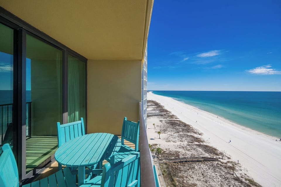 Sunlight sparkles on the coastline as you watch lively beachgoers from your balcony