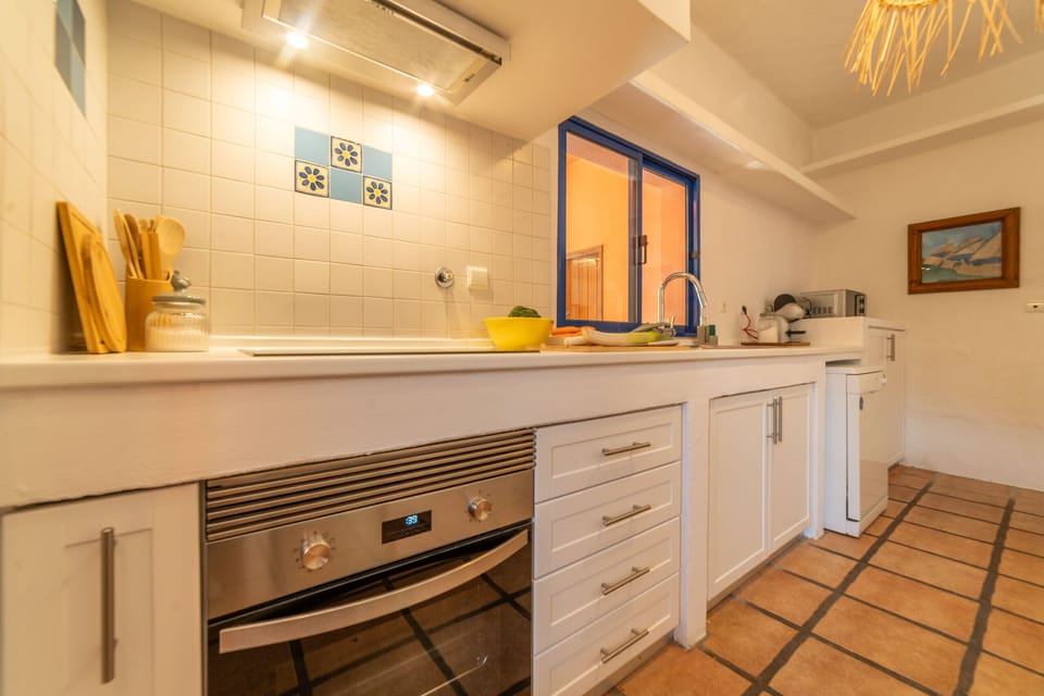 Modern kitchen with white cabinetry and blue-framed window — Villa Bambu, holiday villa in Herdade de Aroeira