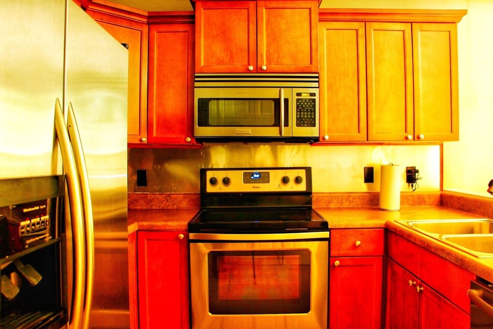 Fully stocked kitchen with microwave, flat top stove, oven, pots, pans, serving utensils, full set of knives with sharpener, dish set, eating utensils, glasses, coffee mugs, stemless wine glasses, retro blender, toaster oven, and toaster.
