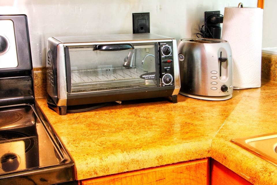 Fully stocked kitchen with microwave, flat top stove, oven, pots, pans, serving utensils, full set of knives with sharpener, dish set, eating utensils, glasses, coffee mugs, stemless wine glasses, retro blender, toaster oven, and toaster.