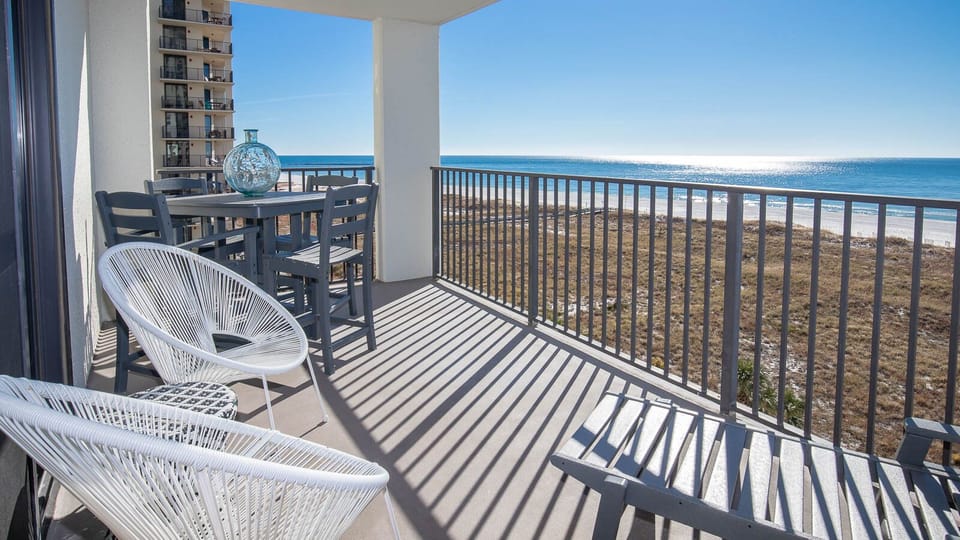 Balcony features a dining table with chairs and two stylish white chairs, overlooking the beach and sparkling gulf waters