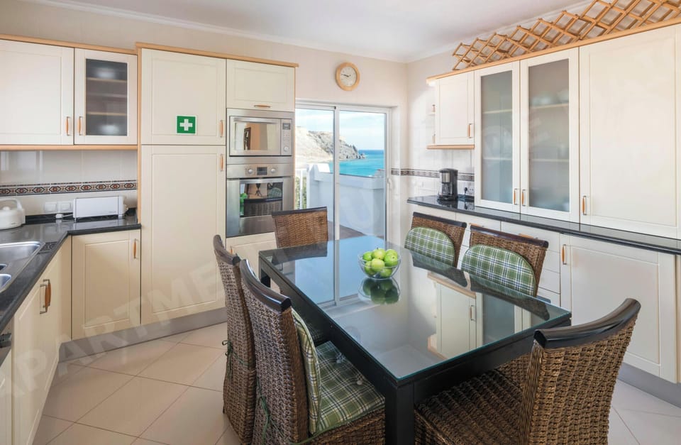 Open-plan dining area with sea views through the balcony doors at Rua 1º de Maio apartment in Praia da Luz, featuring a dining table and adjacent kitchen area