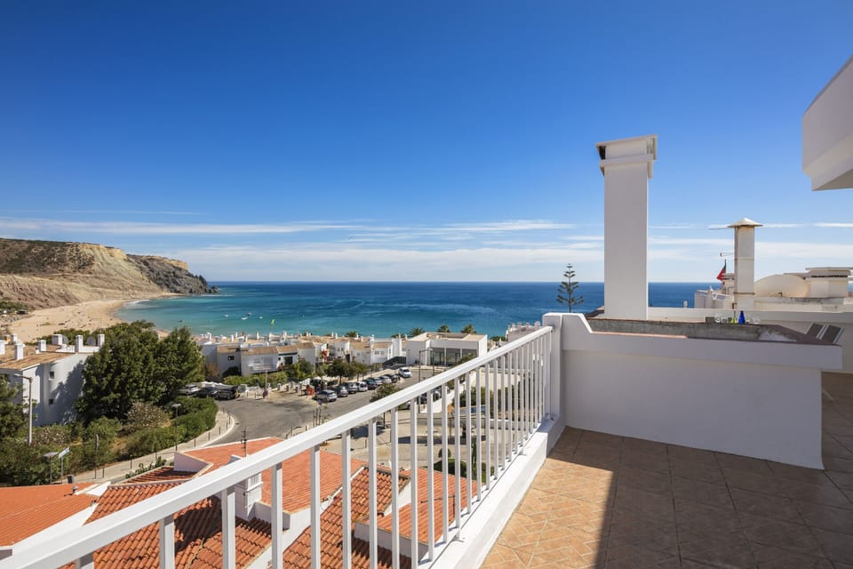 Breathtaking balcony view from Rua 1º de Maio apartment overlooking Praia da Luz beach, dramatic golden cliffs, and the sparkling Atlantic Ocean, perfect for enjoying stunning Algarve sunsets