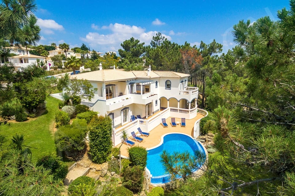 Private swimming pool at Casa Clajon villa surrounded by tropical gardens and palm trees, with the whitewashed villa and sun terraces overlooking the Algarve golf course near Carvoeiro