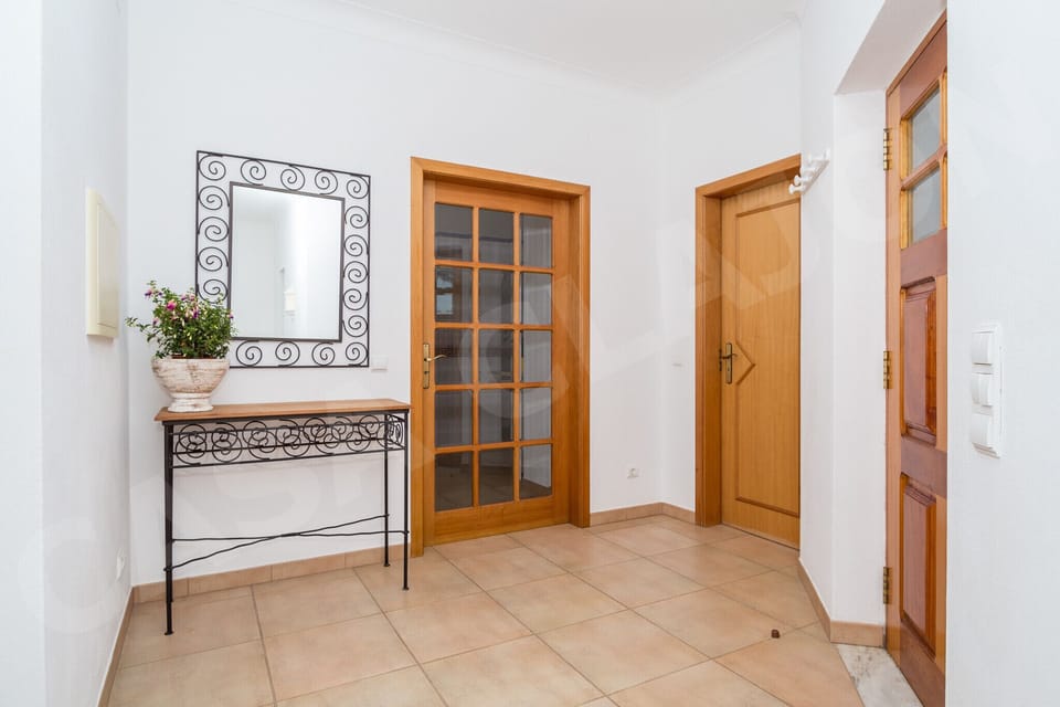 Welcoming entrance hallway at Casa Clajon holiday villa near Carvoeiro, Algarve, with a decorative wrought iron console table, mirror, and traditional wooden door with glass panels. The tasteful details throughout this 4-bedroom villa reflect the charm of Portuguese holiday living.