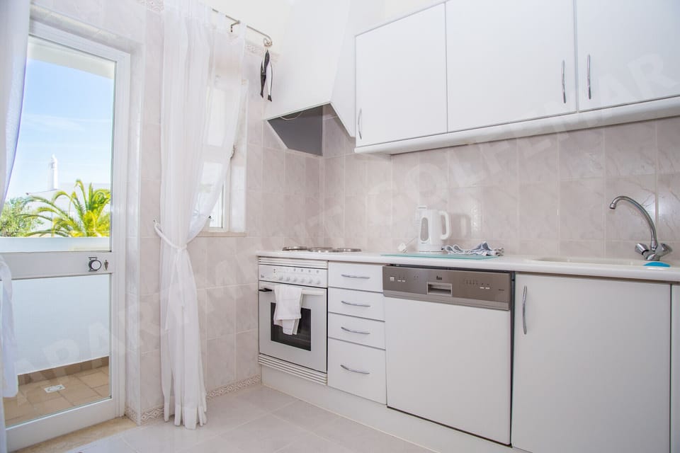Bright kitchen area in Vila Golfemar apartment with white fitted units, ample worktop space, and a window bringing in natural Algarve sunlight, ideal for preparing holiday meals