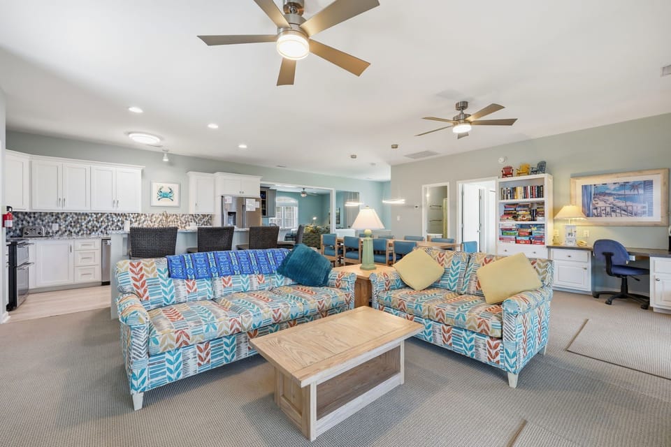 Settle into your bright open-plan retreat where vibrant coastal-themed sofas invite relaxation, the kitchen awaits your culinary creations, and ceiling fans keep every corner refreshingly cool.