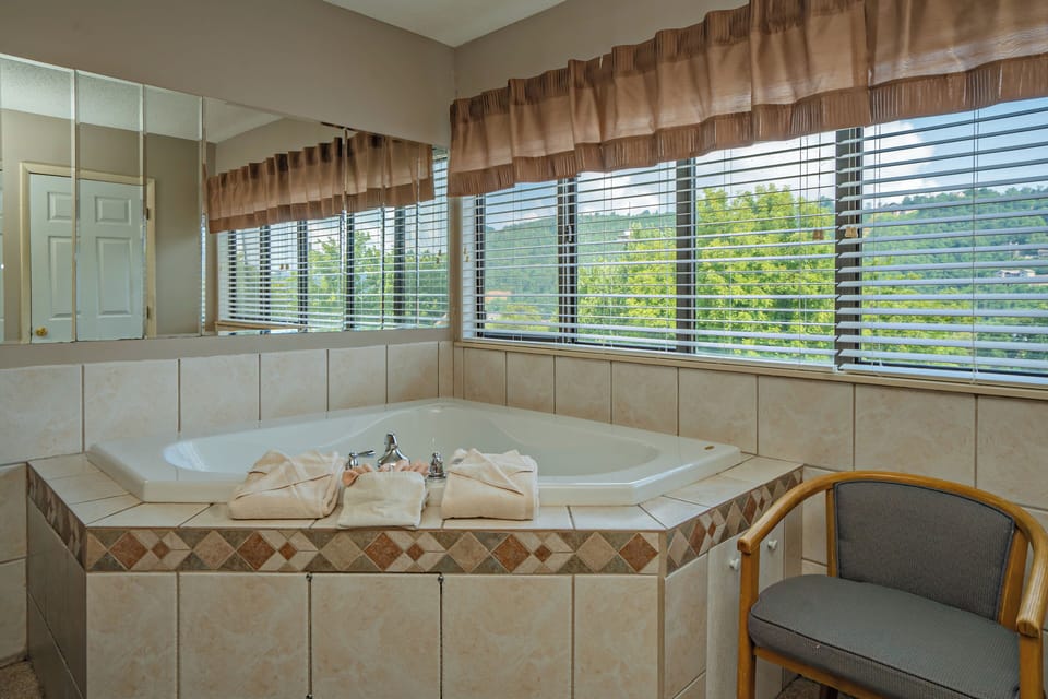 Sink into relaxation in your private soaking tub framed by sunlit windows. Natural light filters through blinds, overlooking peaceful greenery while you unwind with soft towels and peaceful views.