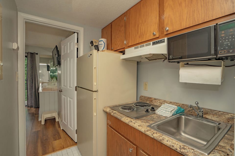Your compact kitchen has everything you need: a full-size fridge, microwave, electric stove, and stainless sink. Warm wood cabinets and granite-style countertops keep it inviting and practical.