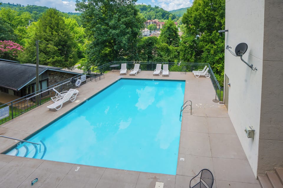A sparkling pool surrounded by lush trees and mountain views, nestled in a scenic hillside setting. The peaceful surroundings and refreshing water create an ideal retreat.