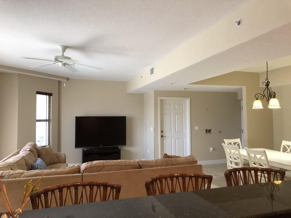 Living room with sectional, flat screen tv, and access to private balcony.