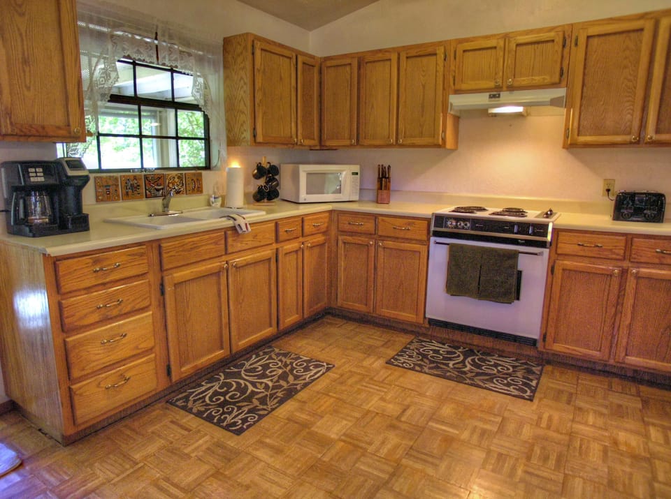 Parquet flooring anchors the kitchen space with oak cabinetry, two patterned rugs, and a coffee maker by the window.
