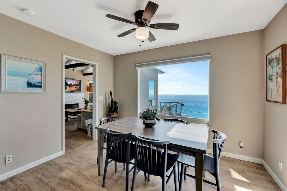 Dining table set beside large windows overlooking the sparkling sea