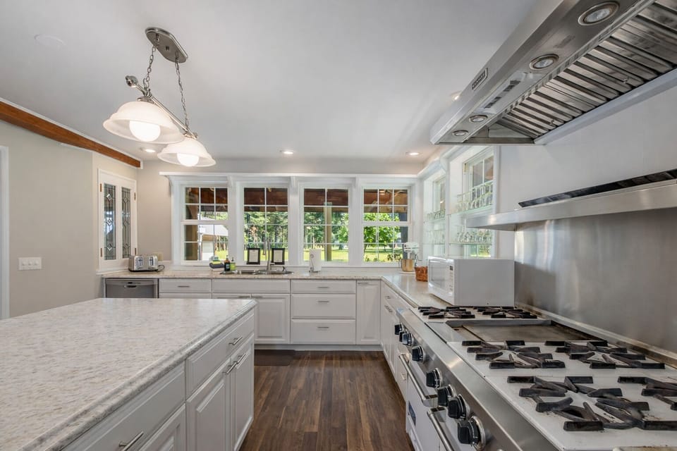 Cook with joy in this bright, fully-equipped kitchen featuring pristine marble counters, professional-grade appliances, and garden views through expansive windows.