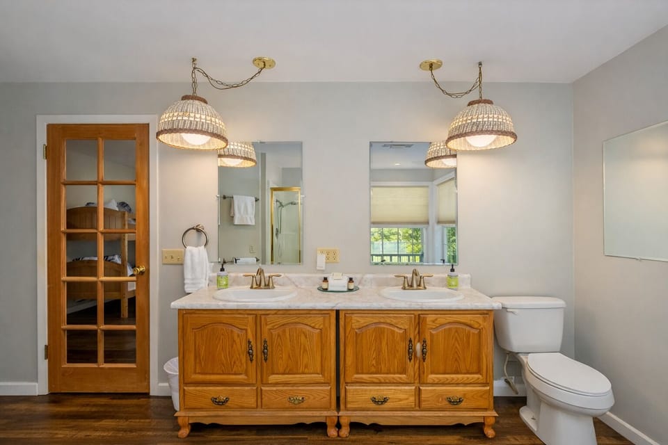 Relax in your elegant master bathroom with warm pendant lighting, dual vanities, and charming vintage-style cabinetry for a perfect morning routine.