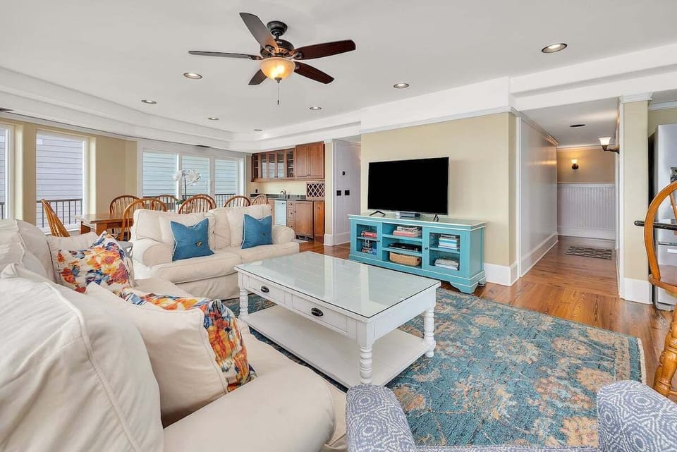 Living room with white sofas, teal accents, ceiling fan, TV
