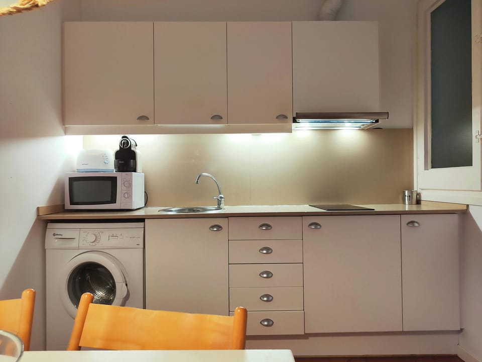 This well-lit kitchen features a microwave, a coffee maker, a toaster, and a washing machine. White cabinets provide ample storage space.