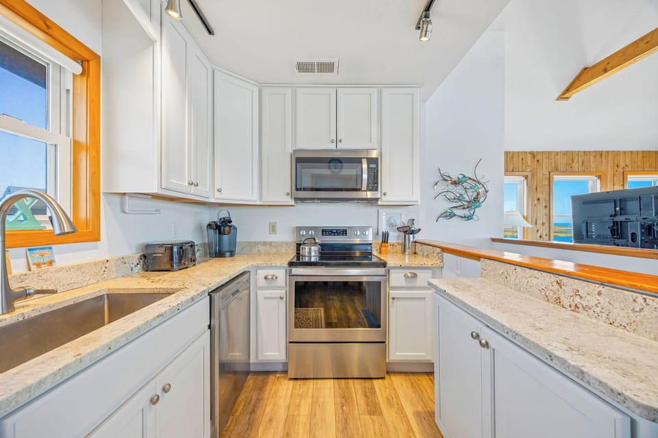 Your fully-equipped kitchen features granite counters, stainless appliances, and ocean views through the pass-through window—perfect for cooking with a coastal backdrop.
