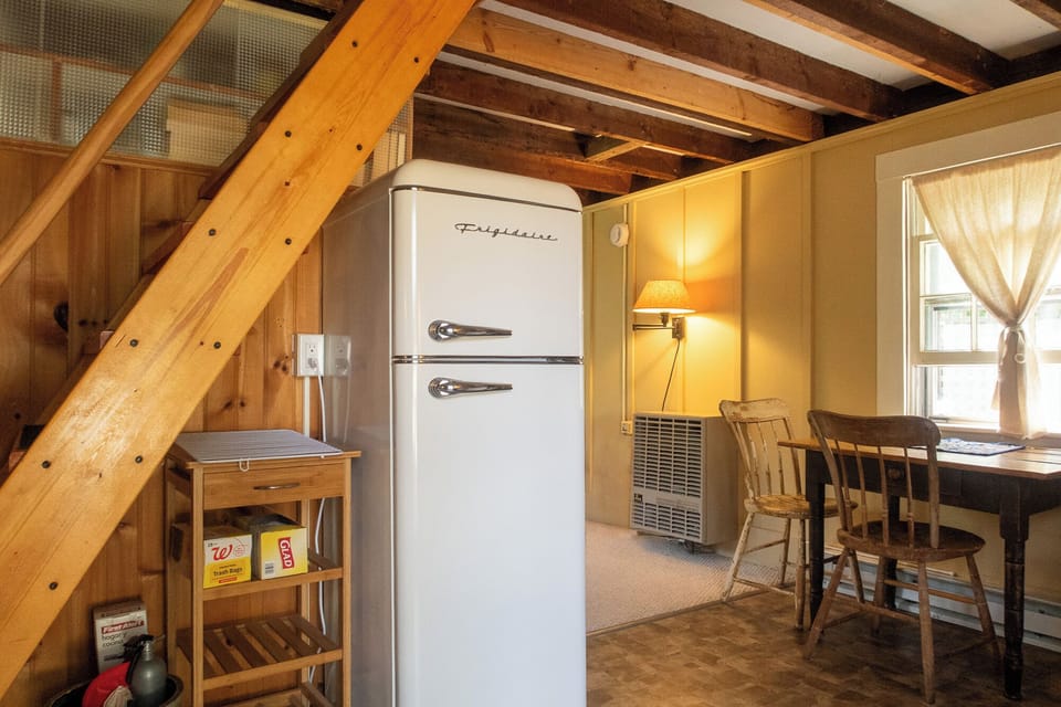 The compact fridge and the dining table next to the sunny window.