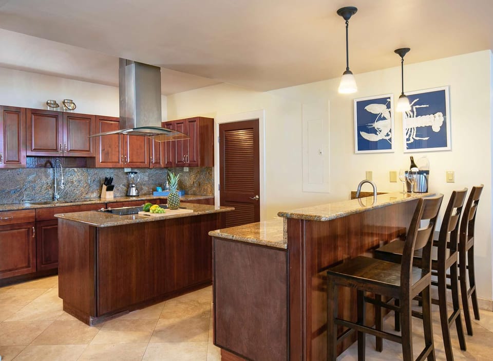 Granite countertops extend across the kitchen island and breakfast bar with three dark wood stools beneath pendant lighting.