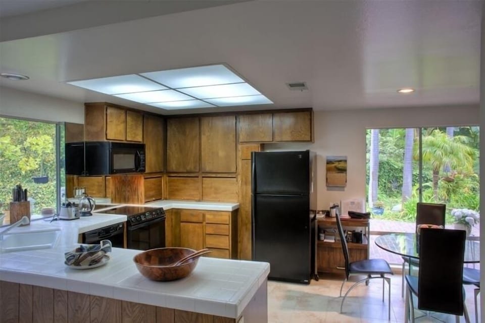 full kitchen, bright, surrounded by windows to the garden, with an eating area.