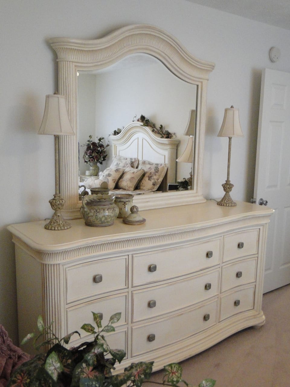 Master bedroom dresser with bed visible through mirror.