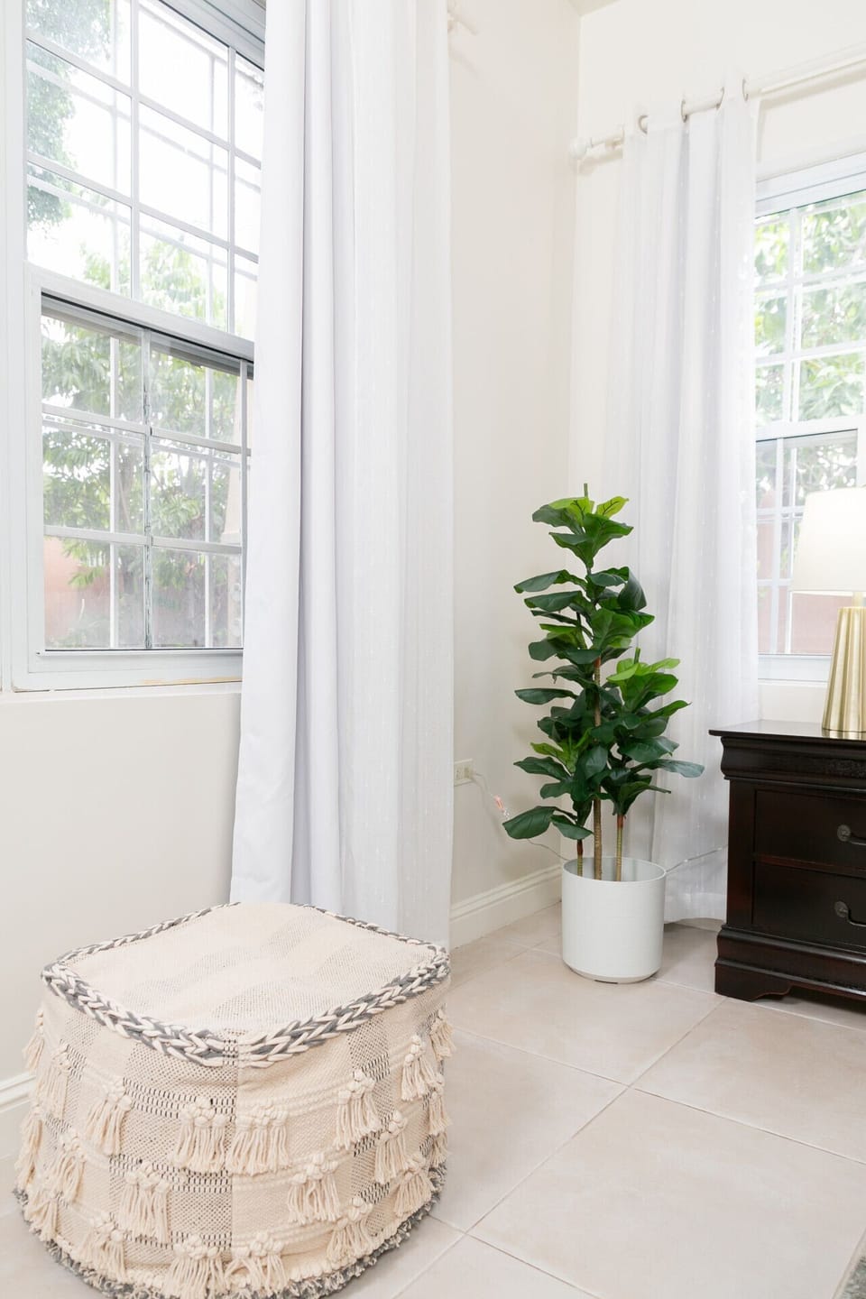 Sunlit corner w/ tall windows, flowing curtains & a leafy indoor plant.