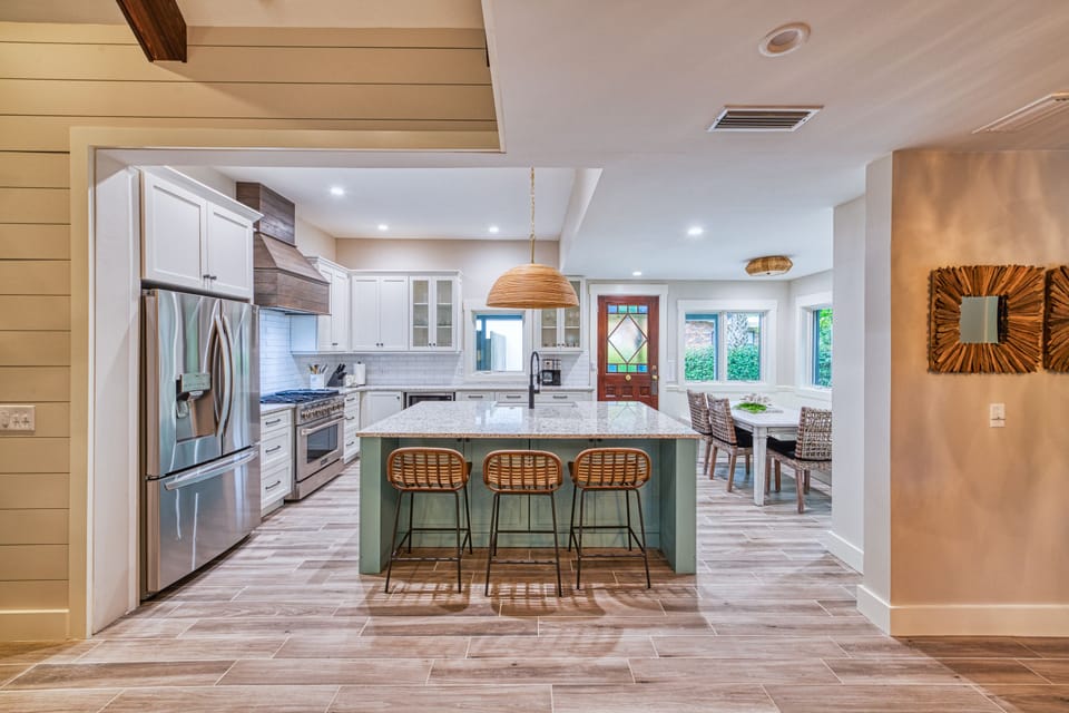 Open Kitchen with Island and Dining Flow – Tabby on 12th - This wide-angle kitchen view highlights the island seating, open sightlines, and clean transition to the dining area and patio. Everything you need for breakfast spreads, seafood dinners, or evening drinks under the lights.