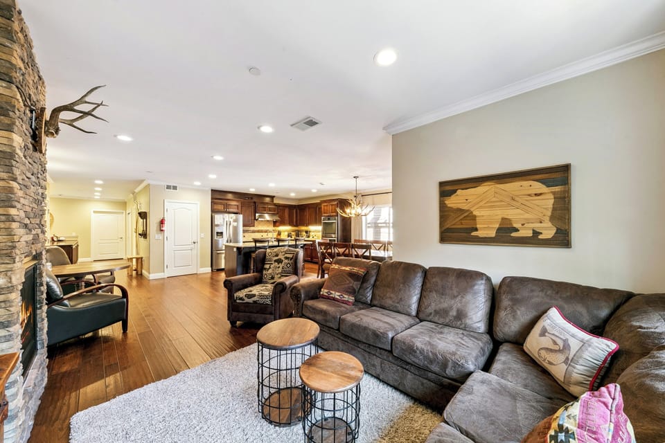 Unwind on the plush leather sectional in your cozy living space, where rustic charm meets modern comfort with stone fireplace and mountain-themed decor.