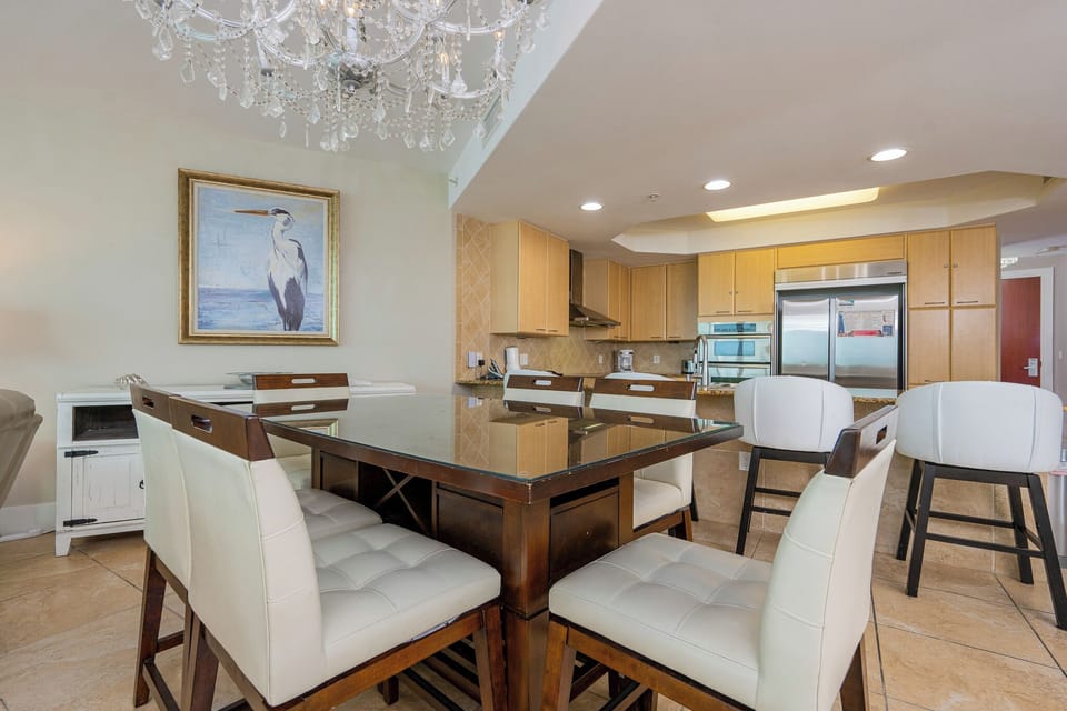 Elegant dining area featuring a glass-top table, plush white chairs, and a stunning chandelier in a modern kitchen setting