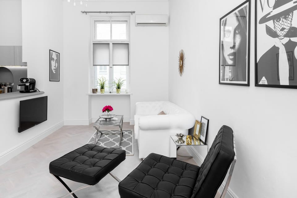 Elegant and stylish living area with a white sofa, a coffee table, an armchair, and a kitchenette.