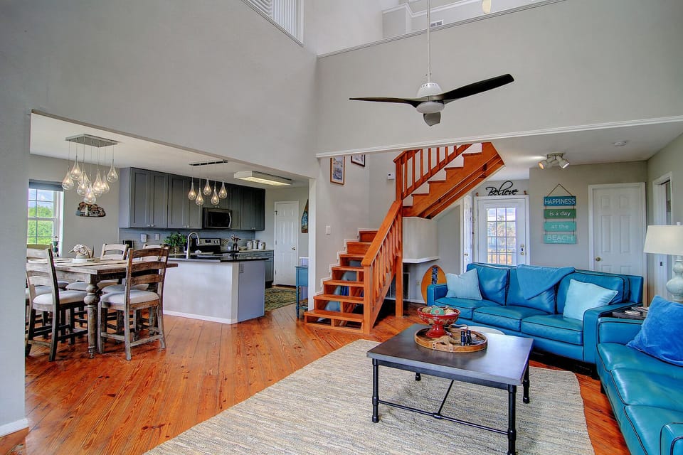 Relax in your spacious open-plan living area with vibrant blue leather seating, modern kitchen, and charming wooden staircase.