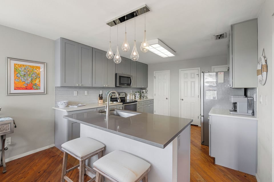 Gather around the sleek kitchen island with modern pendant lighting overhead. Gray cabinetry, stainless appliances, and ample counter space make cooking your favorite meals effortless and enjoyable.