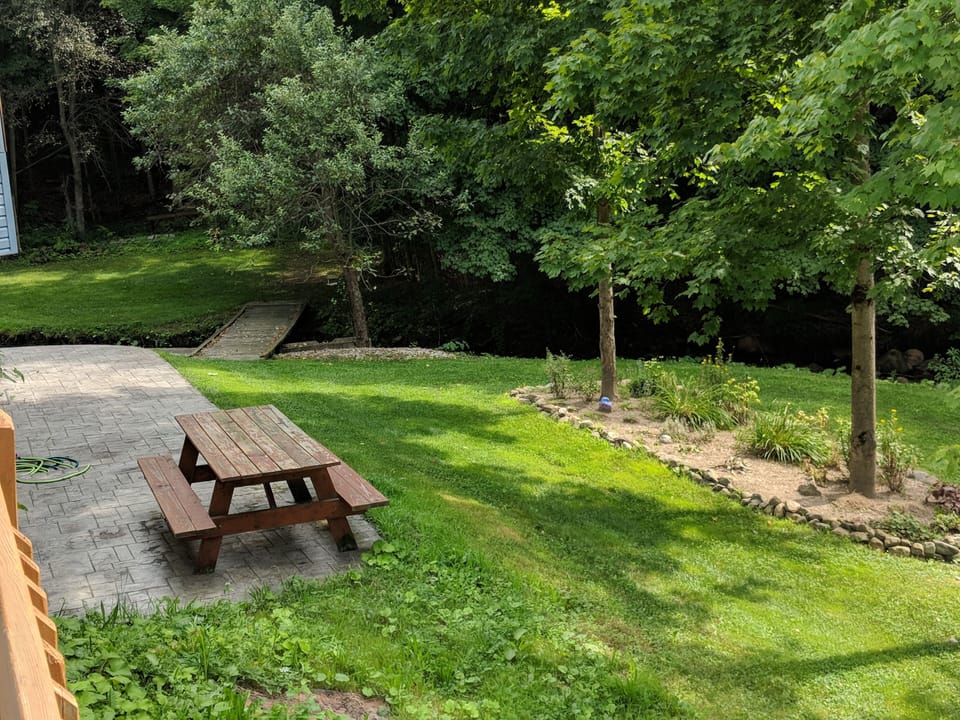 Very large yard for your use with picnic table + bridge over creek to fire pit.
