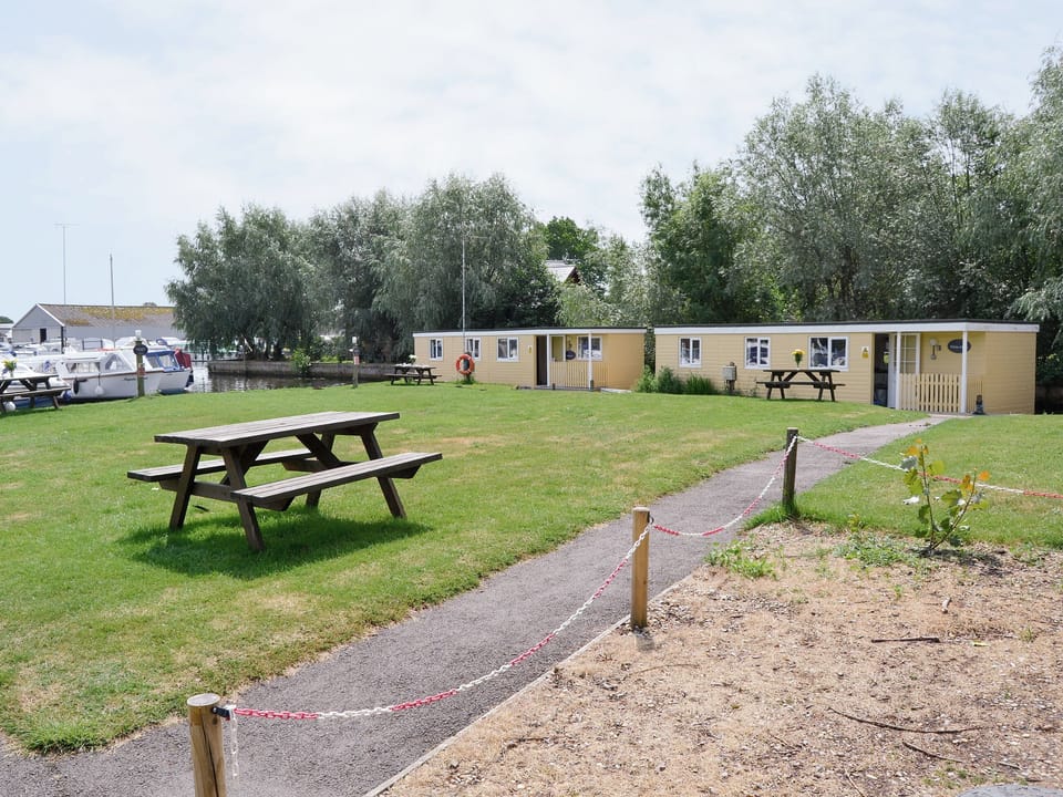 Outdoor seating on the lawned recreation area | Halcyon - Norfolk Riverside Cottages, Stalham